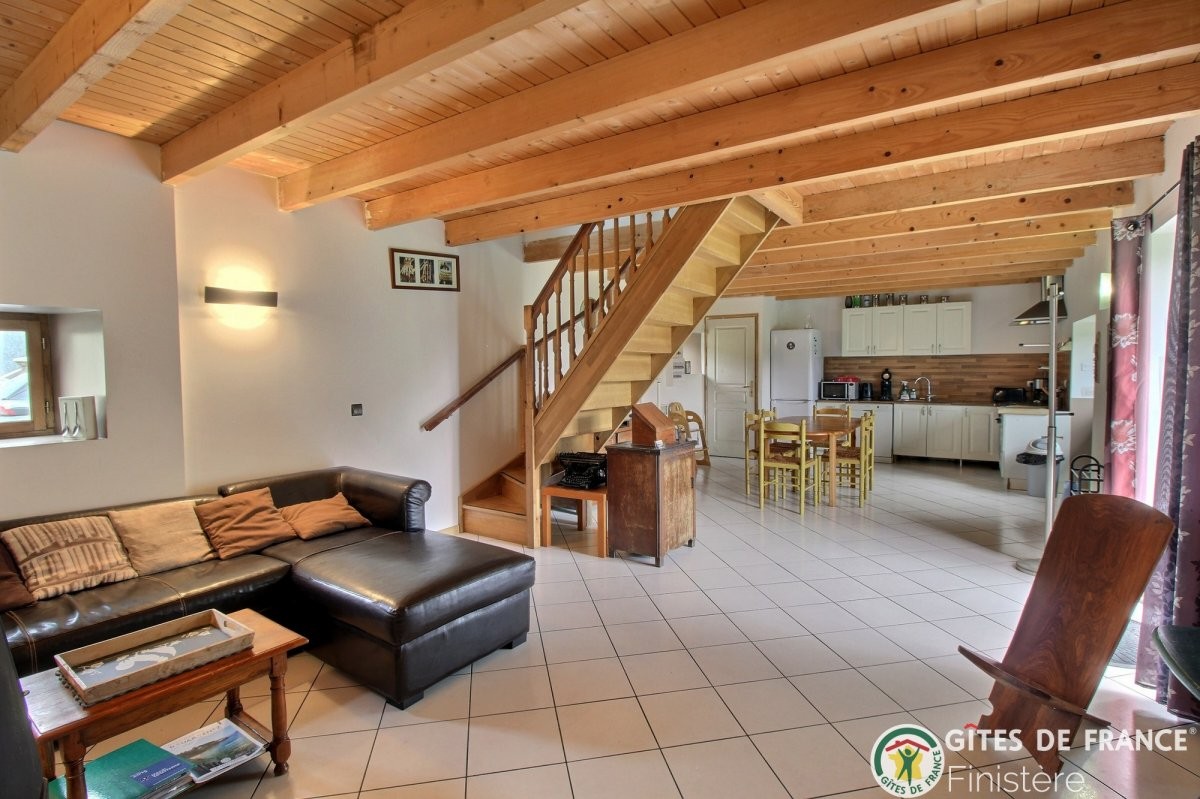 Espace détente spacieux Salon avec un canapé en cuir et une cuisine ouverte, escalier en bois à l'arrière.