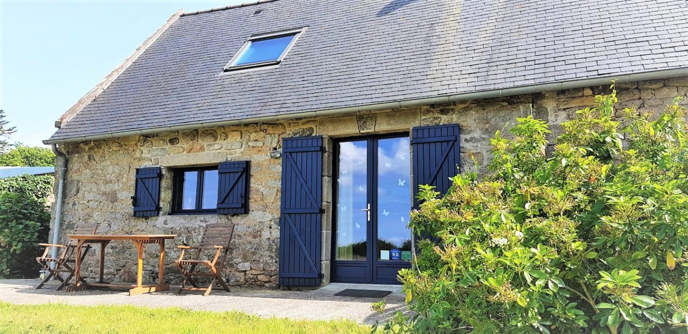 Gîte romantique en Finistere Maison en pierre avec volets bleus, table en bois à l'avant, verdure environnante.