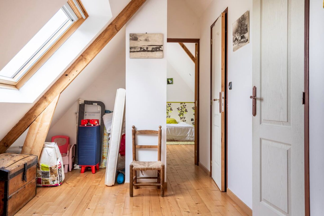 Mezzanine avec espace de jeux pour enfants, desservant 2 chambres, une salle de bain et un wc Couloir lumineux avec des murs blancs, des portes et des meubles en bois.