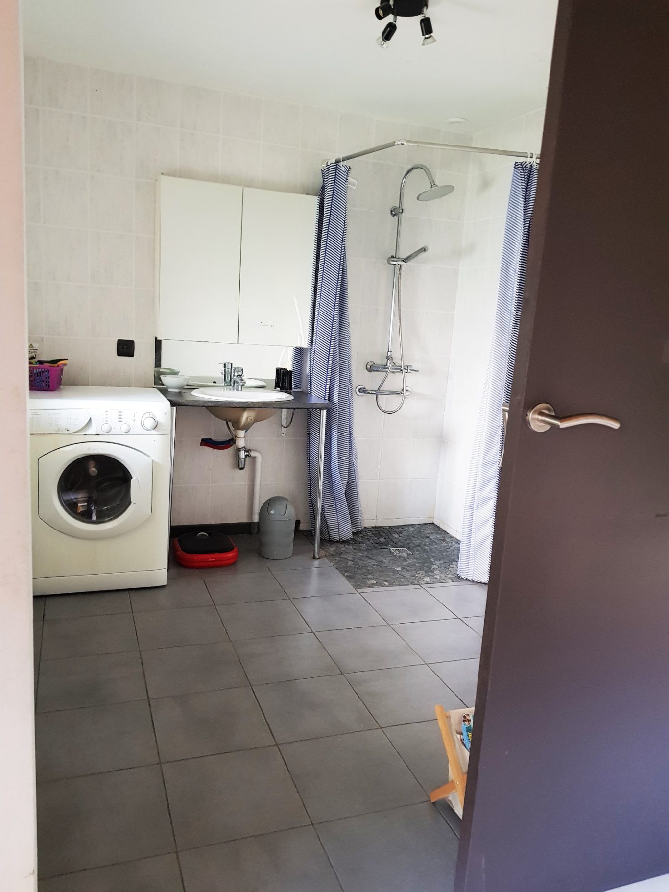 Salle de bain accessible en rez de chaussée Salle de bain avec douche, machine à laver et lavabo sur un sol carrelé.