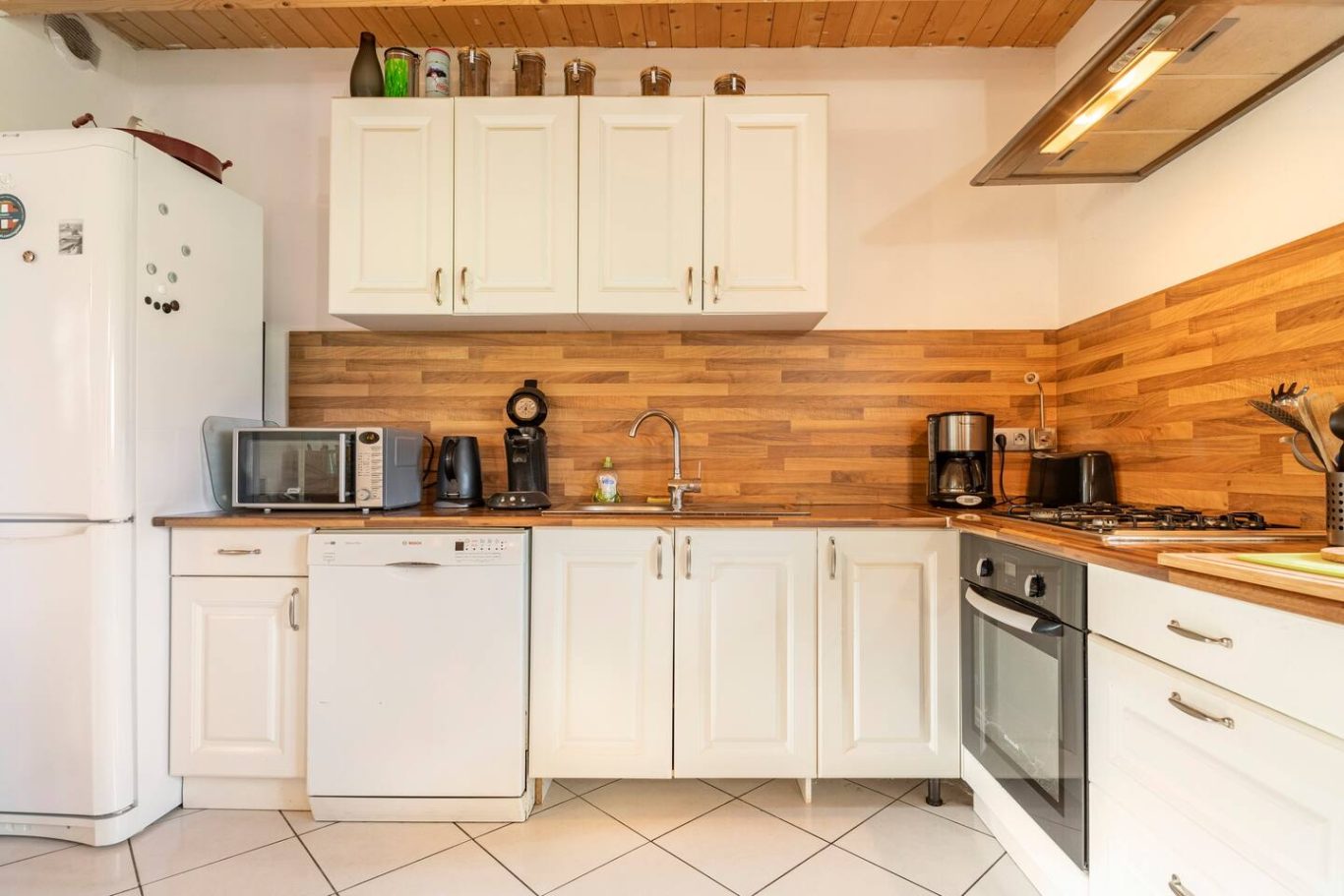 Cuisine moderne et entièrement équipée Cuisine moderne avec meubles blancs et mur bois, équipée d'électroménagers.