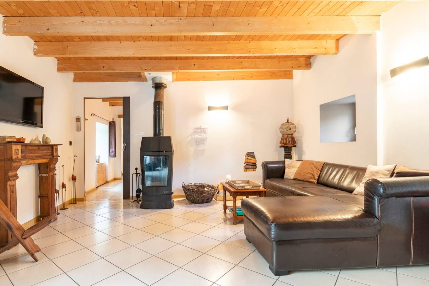 Tv et poêle à bois pour des soirées cosy Salon lumineux avec un canapé, un poêle et des poutres en bois au plafond.